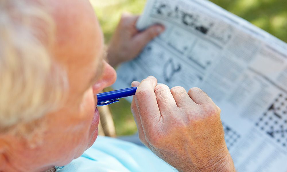 Older man doing the crosswords puzzle in the newspaper to exercise his mind